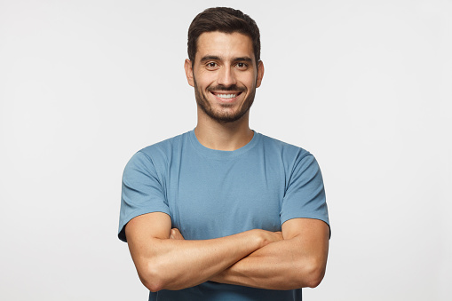 Retrato de sonriente hombre guapo en pie camiseta azul con brazos cruzados aislados sobre fondo gris photo