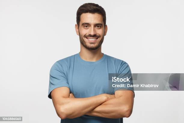 Retrato De Sonriente Hombre Guapo En Pie Camiseta Azul Con Brazos Cruzados Aislados Sobre Fondo Gris Foto de stock y más banco de imágenes de Hombres