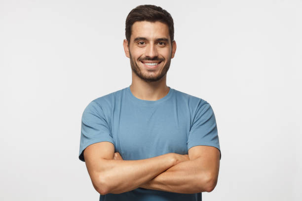 ritratto di bell'uomo sorridente in t-shirt blu in piedi con le braccia incrociate isolate su sfondo grigio - arto umano foto e immagini stock