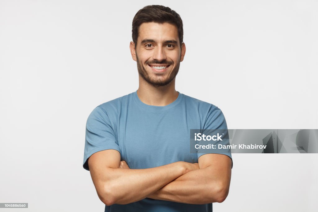 Portrait of smiling handsome man in blue t-shirt standing with crossed arms isolated on grey background Men Stock Photo