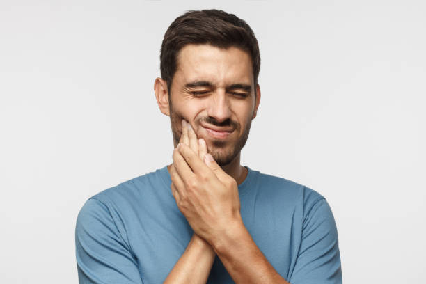 istock Tooth ache. Young man feeling pain, holding his cheek with both hands, suffering from bad toothache, having painful expression 1045886588