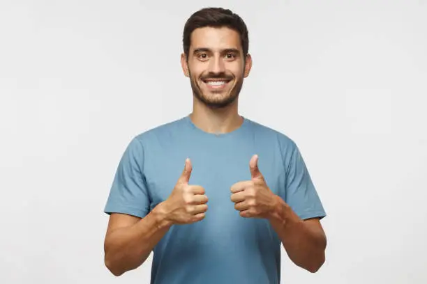 Motivated excited smiling young man in blue t-shirt, making thumbs up gesture of approval and success