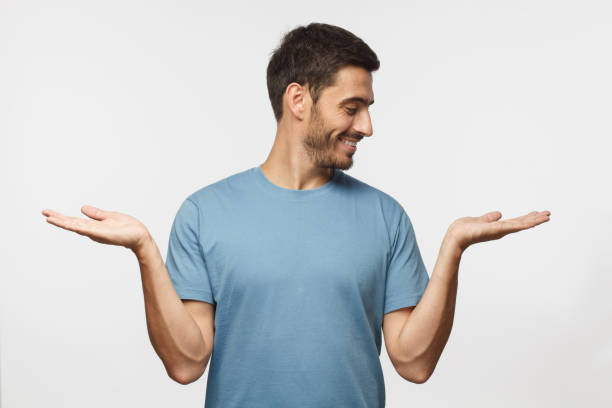 istock Young handsome male choosing between two different options, holding 2 hands, isolated on gray background 1045886638