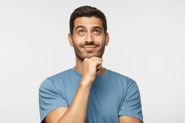 junger mann im blauen t-shirt mit verträumten fröhlichen ausdruck, denken, blick nach oben, auf grauem hintergrund isoliert - moving up looking men people stock-fotos und bilder