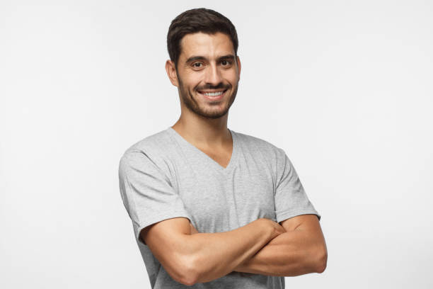 портрет привлекательного молодого спортивного мужчины в серой футболке, стоящей со скрещенными руками, изолированным на сером фоне - male fashion model adult human arm стоковые фото и изображения