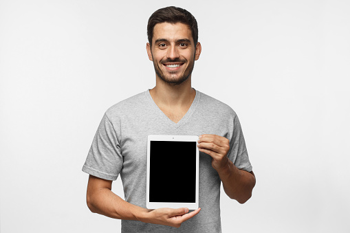 Joven que presenta tablet en blanco vertical de la pantalla a los espectadores con sonrisa, espacio de copia para publicidad de bienes o de la aplicación, aislado sobre fondo gris photo