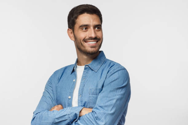 Handsome young man isolated on gray background, dressed in casual blue shirt, having turned aside as if looking at something