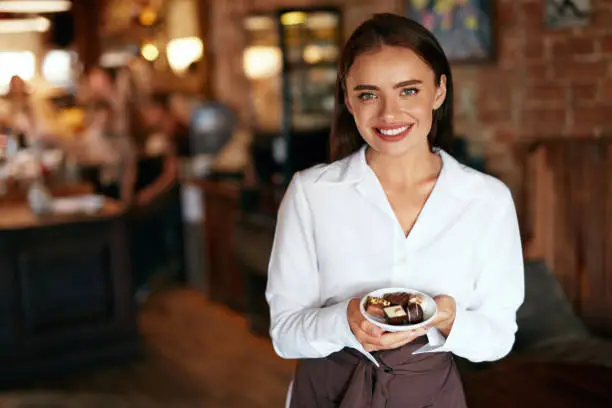 Waitress In Cafe. Beautiful Woman With Chocolate Candies In Confectionery Store. High Resolution