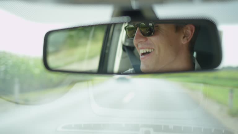 SLOW MOTION: Happy Caucasian man sings while driving through the countryside.