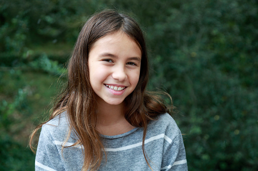 Portrait of happy preteen child kid smiling friendly, glad expression looking at camera dreaming, resting, relaxation feel satisfied good news. Pretty blonde girl on city sunset park street, outdoors