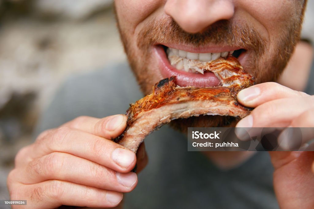 Ihmiset syövät ruokaa. Mies syö grillikylkeä grillibaarin lähikuvassa - Rojaltivapaa avainsanalla Grilli ja tyyppiä Kuvapankin valokuva