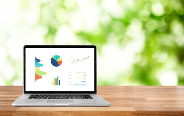istock Modern laptop on wooden table showing charts and graph against s blurred blue modern buildings and sky background 1045942128