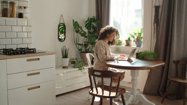 istock Charming young woman typing on laptop computer in a kitchen. 1045960338