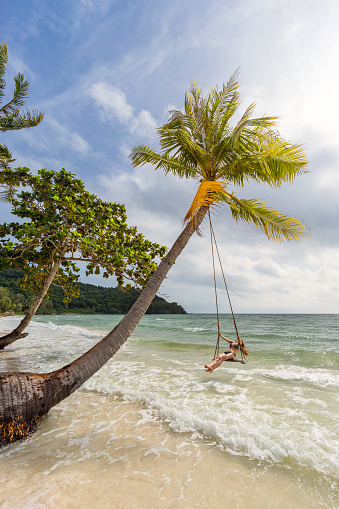 Young woman on a swing on exotic tropical sandy Bai Sao beach in the sea under a palm tree