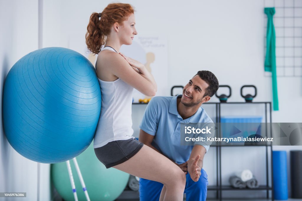 Smiling professional personal trainer helping sportswoman exercising with ball Physical Therapy Stock Photo