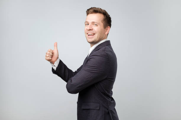 portrait of excited man in suit giving thumb up against gray background - thumbs up business people isolated imagens e fotografias de stock