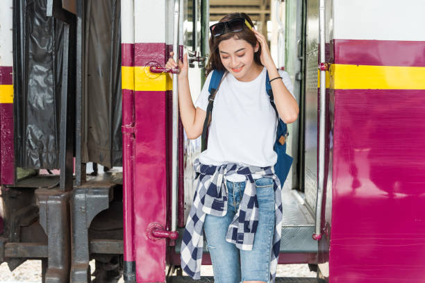 Smiling young tourist woman with blue backpack stepping down to the train at railway station. Travel concept stock photo