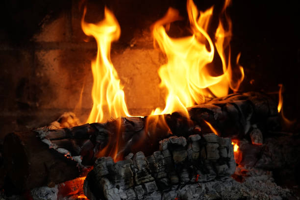 Burning firewood in the fireplace close-up. Close-up with burning logs and vivid burning orange and yellow flames. Flames crawl up the side of a piece of firewood in an open campfire.