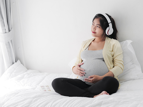 Asian pragnant woman using headphone listening music on bed, lifestyle concept.