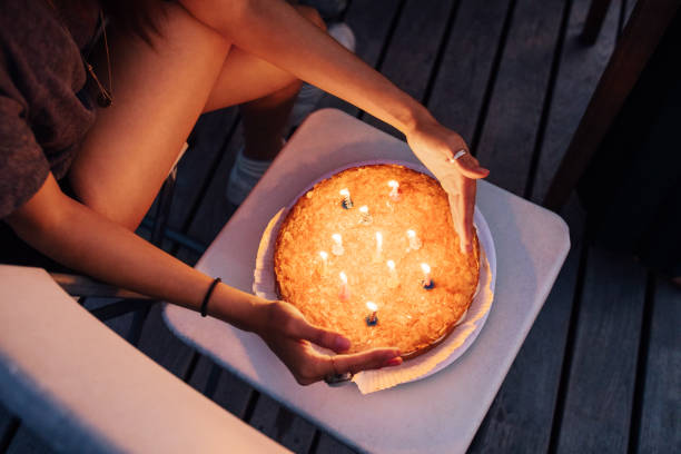 Top view of woman hands protecting burning candles on cake on chair. Female with a birthday cake on roof.