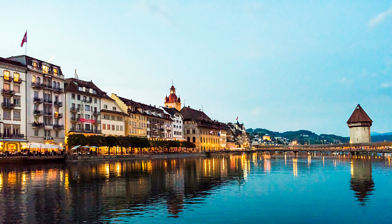 View of Chapel Bridge on River Reuss with Lucerne city skyline at sunset in Switzerland.