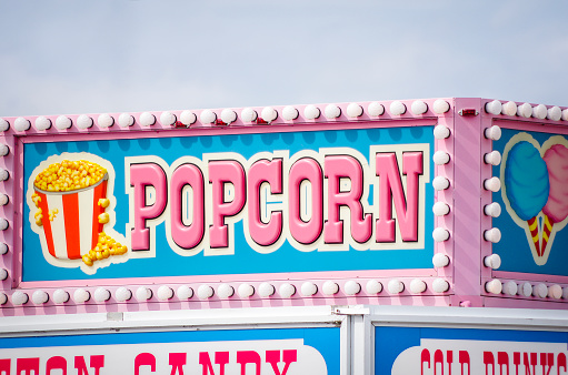 Brightly coloured popcorn concession sign at a summer carnival, with blue sky background.
