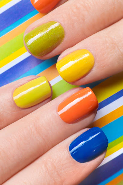 Colorful bright manicure with orange, blue, yellow nail Polish Colorful bright manicure with orange, blue, yellow nail Polish on striped background close-up.Nail art. yellow nail polish stock pictures, royalty-free photos & images