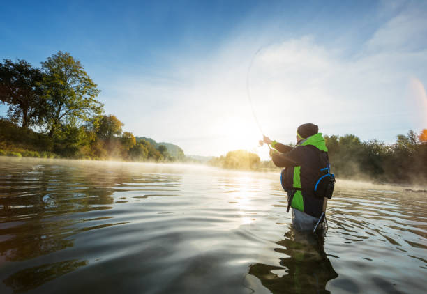 istock Fisherman holding fishing rod, standing in river 1046036498