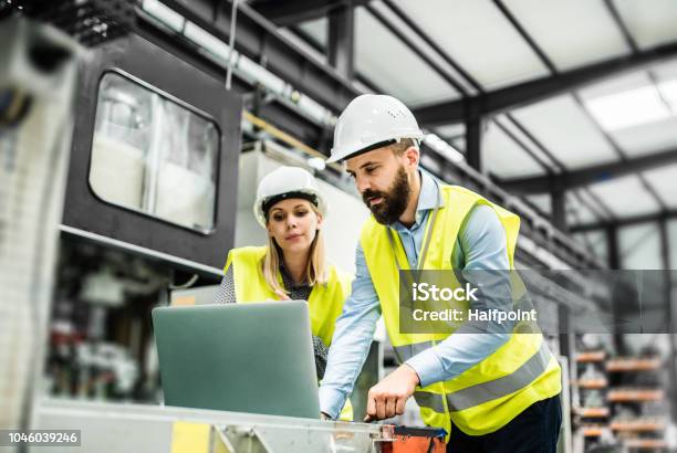 Un Retrato Del Ingeniero Industrial Del Hombre Y La Mujer Con El Portátil En Una Fábrica Trabajando Foto de stock y más banco de imágenes de Manufacturar