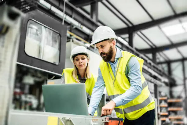 Photo of A portrait of an industrial man and woman engineer with laptop in a factory, working.