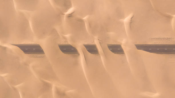 aerial view of a desert road being run over by sand dunes. - liwa desert imagens e fotografias de stock
