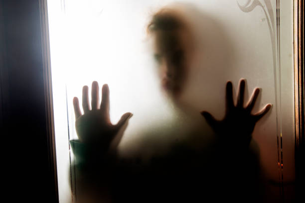 istock Scared person looks through a glass frosted window 1046072244