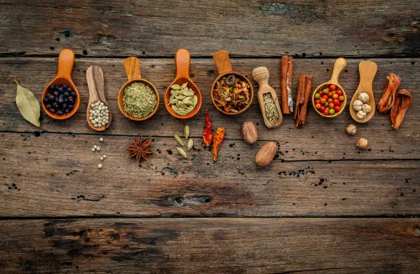 Photo of Various herbs and spices in wooden spoons on wooden background.