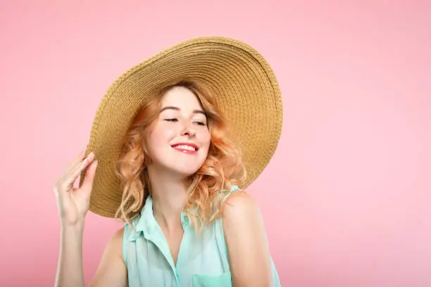emotion expression. smiling happy woman pleased with herself. self-satisfied young beautiful girl in a sunhat. summer beauty and fashion concept. portrait on pink background.