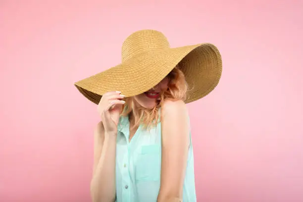 emotion expression. smiling happy mysterious woman pleased with herself. self-satisfied young beautiful girl in a sunhat. summer beauty and fashion concept. portrait on pink background.