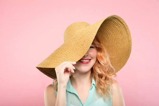 summer vacation tours concept. young pretty woman in a big sunhat ready to go to the beach. cute stylish girl portrait on pink background.