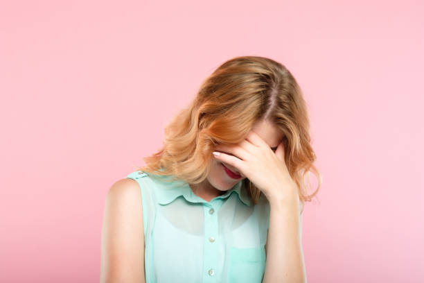 facepalm shame embarrassment girl cover face facepalm embarrassment and shame emotion. ashamed smiling girl covering her face with a hand. young beautiful woman portrait on pink background. embarrassment stock pictures, royalty-free photos & images