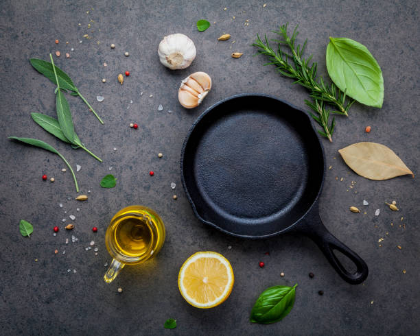 istock Empty old cast iron skillet on dark stone background. Ingredients for making steak  concept with copy space . Various herbs and seasoning rosemary ,sage ,bay leaves ,basil ,garlic and peppercorn. 1046091202