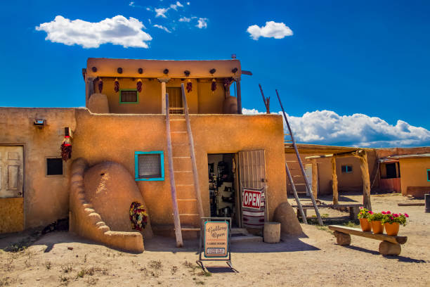 art gallery open at the ancient adobe taos pueblo where indigenous people have lived for over 1000 years - door standing open and flowers set out under beautiful sky - taos imagens e fotografias de stock