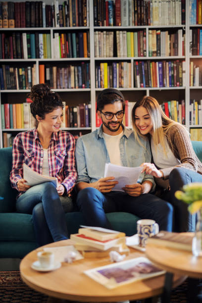 istock Group of three young students sitting in library and preparing exam together. Cheerful teenagers having fun and learning. 1046125722
