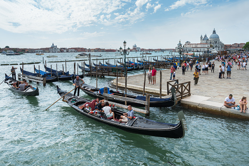 Venice, Italy – August 30, 2018: Gondollas are being oared into the canal of Venice. In the background San Giorgio Maggiore church can be seen.