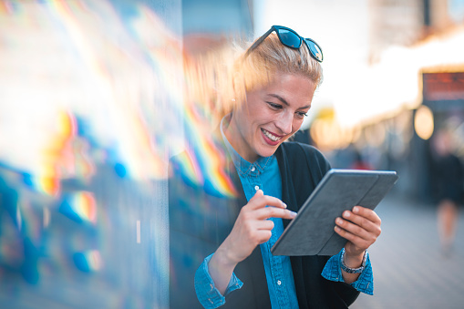 Young woman working outdoors with digital tablet in her hands. She is happy and she is smiling.