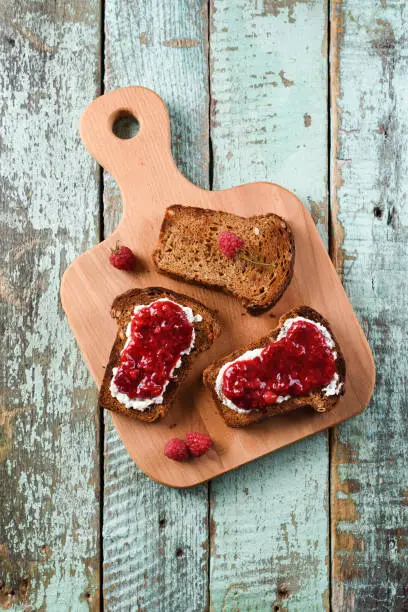 Homemade berry jam with fresh raspberries and currants on rye bread toasts on wooden cutting boards overhead view