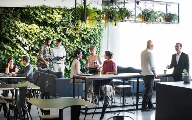 Groups of people meeting around the tables and couches of a trendy office building with a vertical green garden wall