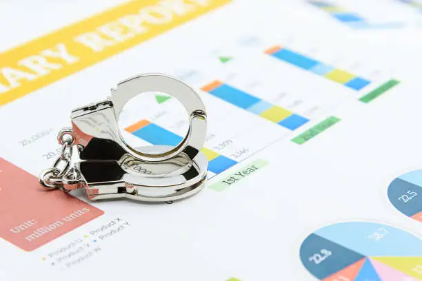 Photo of Business fraud and corporate or company scandal concept : Silver handcuff on an insight, financial highlight with chart or annual analysis report, depics decreased in accountability of auditing firms.