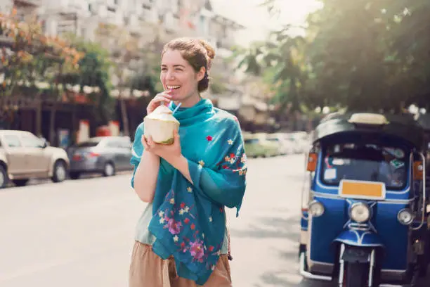 Caucasian female tourist exploring streets of Bangkok and drinking coconut milk.