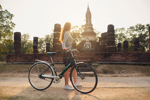 Caucasian female tourist sightseeing Sukhothai historical park on a bicycle.