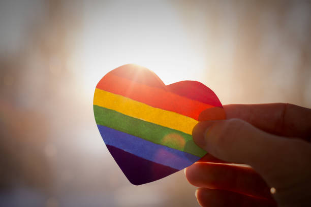 lgbt rights concept, hand holds a heart painted like a LGBT flag, silhouetted against sun lgbtqia pride event photos stock pictures, royalty-free photos & images
