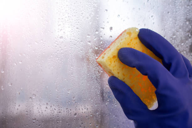 istock Hand blue glove washes window with yellow sponge. 1046252120
