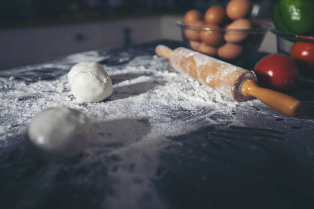 istock Asian women preparing a pizza, knead the dough and puts ingredients on kitchen table 1046288438